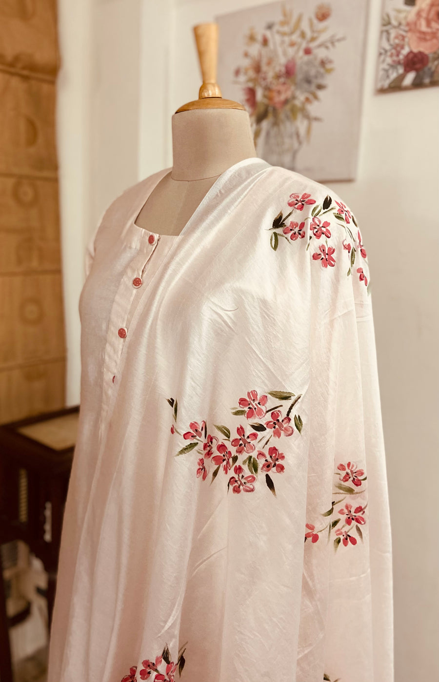 This Lovely suit set is done in pastel peach colour in pure silk chanderi and lined with fine mulmul. The dupatta is also in pure silk chanderi and is handpainted with deep pink daisies all over. Its a three piece suit set.Mulmul And More by Priyanka Bhambry